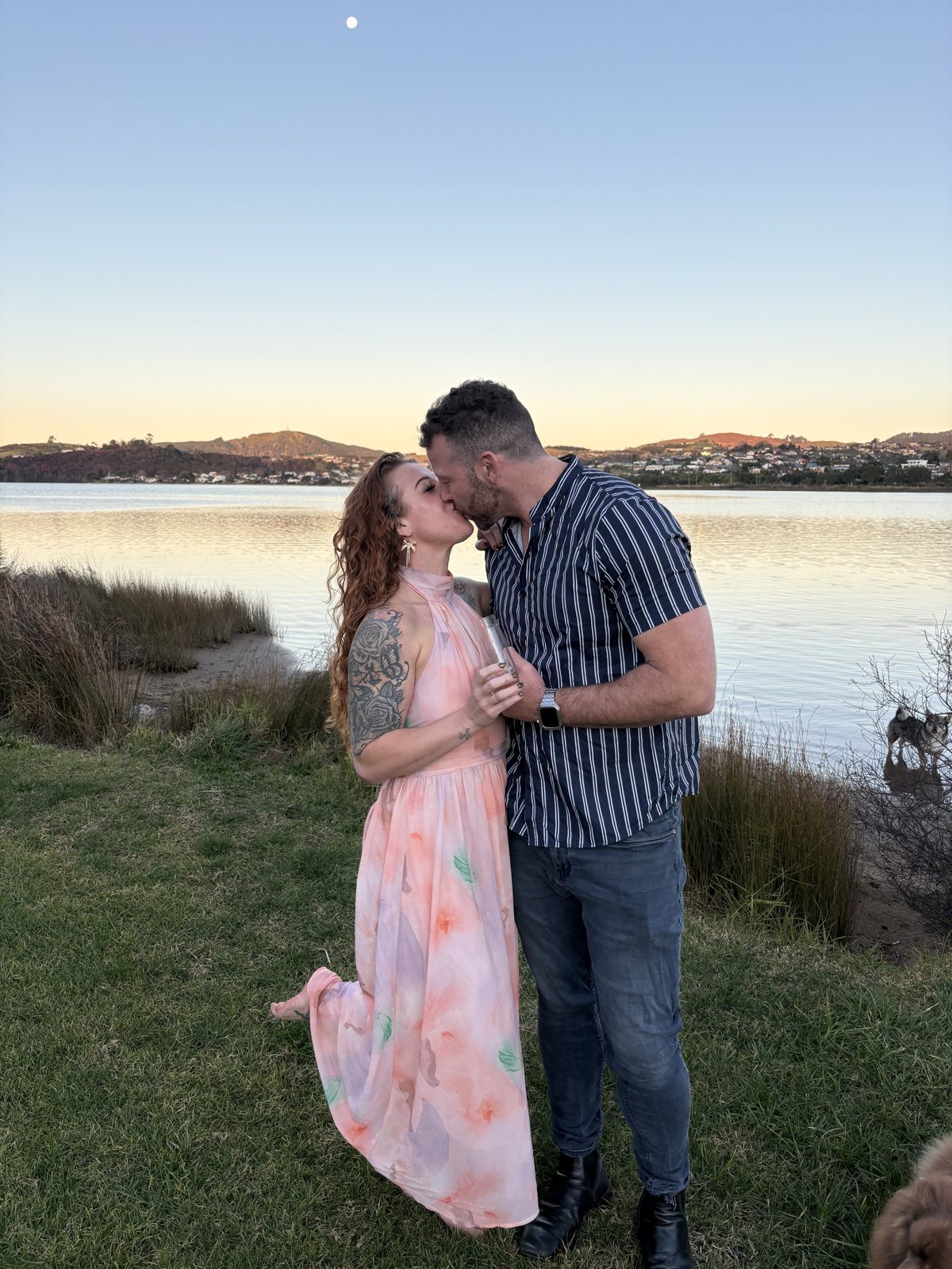 Alex and Dani sharing a kiss beside the lake at golden hour